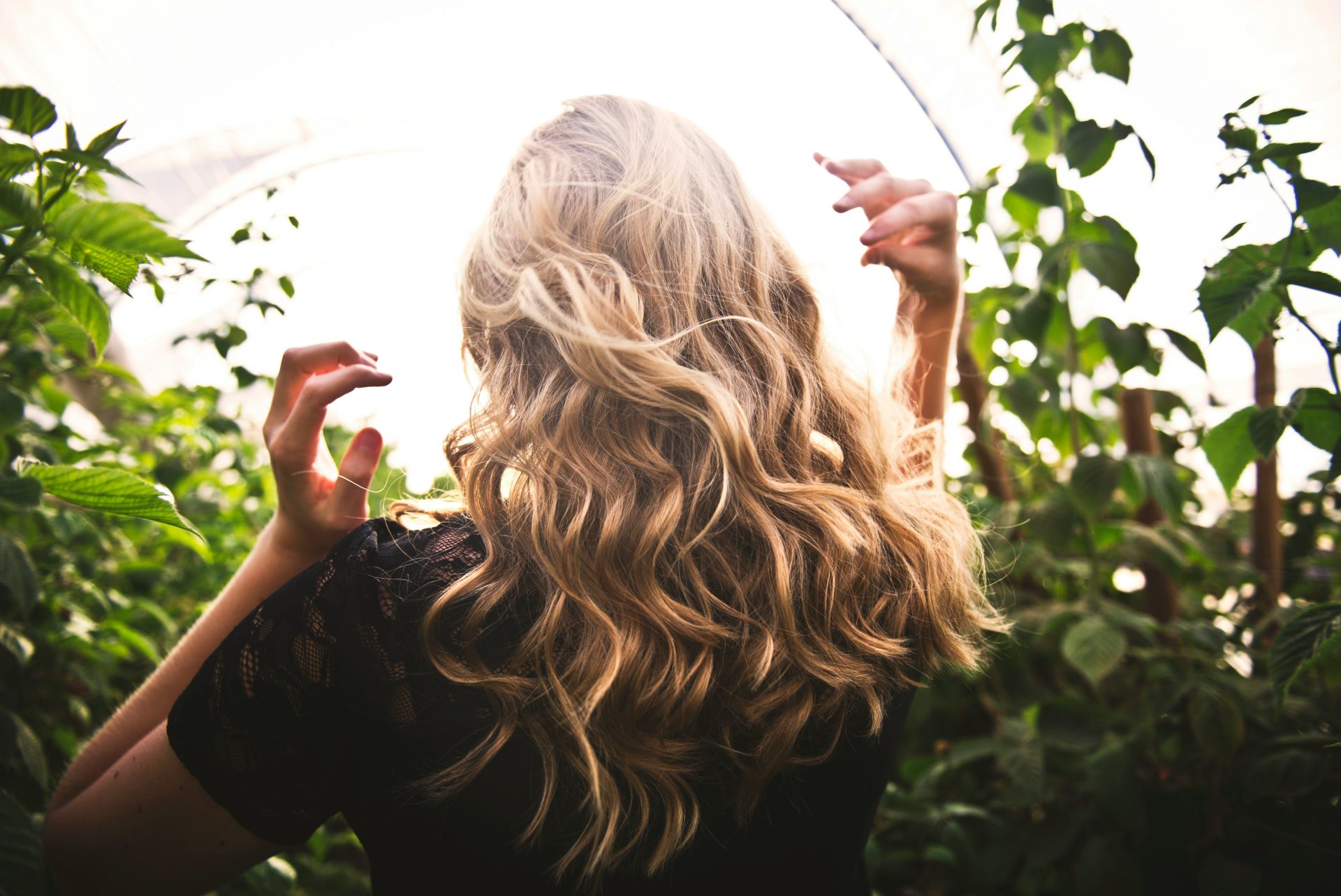 Mujer rubia con top negro rodeada de plantas altas